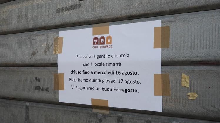 Serrande giù: un cartello affisso alla saracinesca di un esercizio chiuso per ferie COLORFOTO