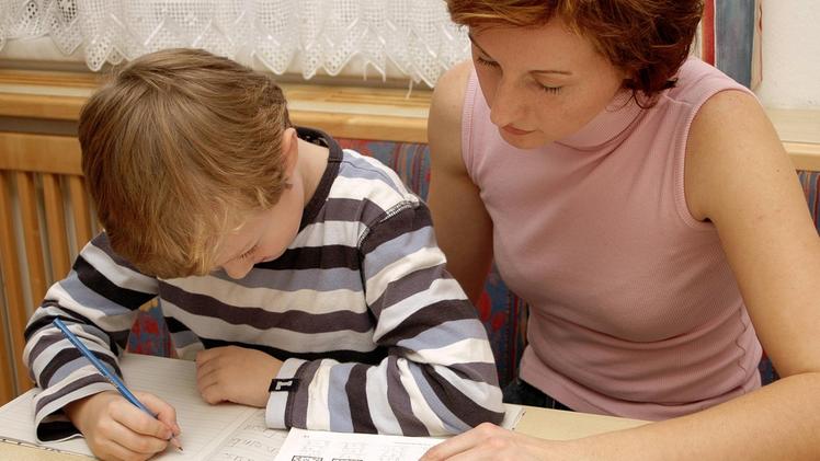 Una signora aiuta un bambino a fare i compiti mentre la mamma è al lavoro. ARCHIVIO